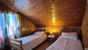Et hyggeligt soveværelse på loftet med trævægge og skrå vægge, med to enkeltsenge og et lille bord med en lampe.