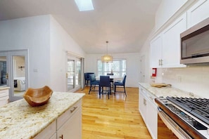 A modern kitchen with a wooden dining table, chairs, and a large window. - Salty Way (Ocean Pines)
