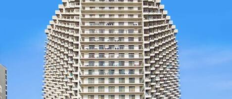 A high-rise building with a unique angular design, multiple balconies, and a clear sky background.