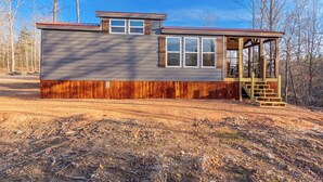 A cabin with a wooden exterior, a covered porch, and a dirt ground.