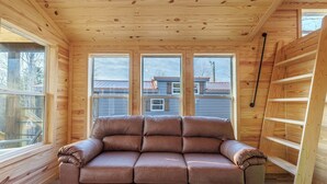 A wooden interior with a sofa, windows, and a ladder.