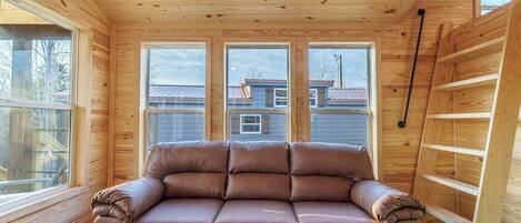 A wooden interior with a sofa, windows, and a ladder.
