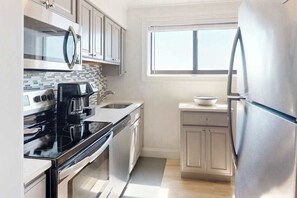 A kitchen with a microwave, stove, refrigerator, and a window. - Camelot 501B (Ocean City)