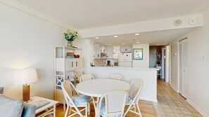 A compact kitchen with white cabinets, a central island, and a dining area with a round table and chairs. - Serene oceanfront condo with beach views, pools, gym, tennis & sauna (Ocean City)
