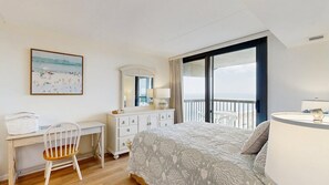 A bedroom with a bed, a desk, a chair, a dresser, a mirror, and a view of the sea. - Serene oceanfront condo with beach views, pools, gym, tennis & sauna (Ocean City)