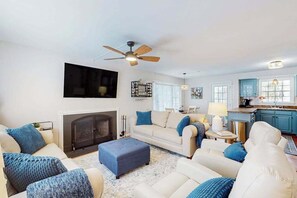 Ein Wohnzimmer mit Kamin, Deckenventilator, einer Sofagarnitur und einer Küchenzeile mit blauen Schränken.