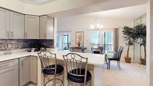A modern kitchen with a central island, bar stools, and a dining area with a chandelier. - 22 Harpoon Rd (Ocean Pines)