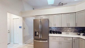 A modern kitchen with a stainless steel refrigerator, light grey cabinets, and a tiled floor. - 22 Harpoon Rd (Ocean Pines)