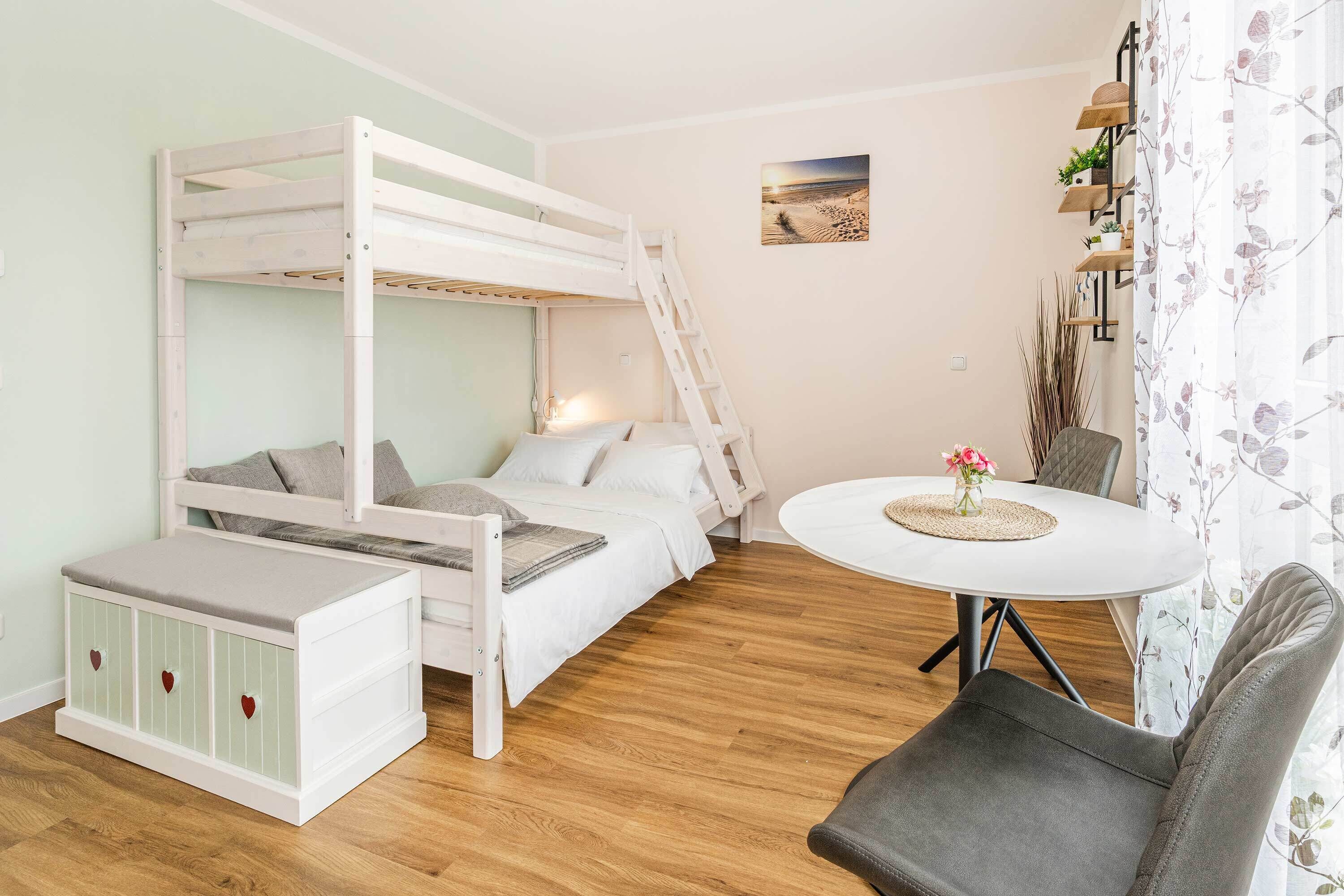 Ein Etagenbett mit Schreibtisch und Stuhl, ein kleiner Tisch mit einer Vase sowie ein an der Wand befestigtes Regal mit Pflanzen.