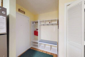 A hallway with a white closet, a bench, and a door with louvered panels. - Sunny Ocean block condo with balcony, AC, WiFi & laundry - walk to the beach (Ocean City)