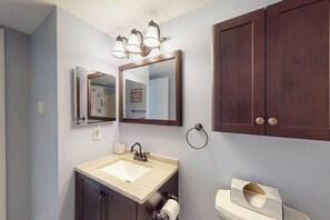 A bathroom with a sink, mirror, toilet, and dark wooden cabinets. - Sunny Ocean block condo with balcony, AC, WiFi & laundry - walk to the beach (Ocean City)