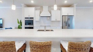 Een moderne keuken met witte kasten, roestvrijstalen apparatuur en een centraal eiland met barkrukken.