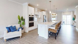 Een moderne keuken met witte kastjes, een centraal eiland en een eethoek met rieten stoelen.