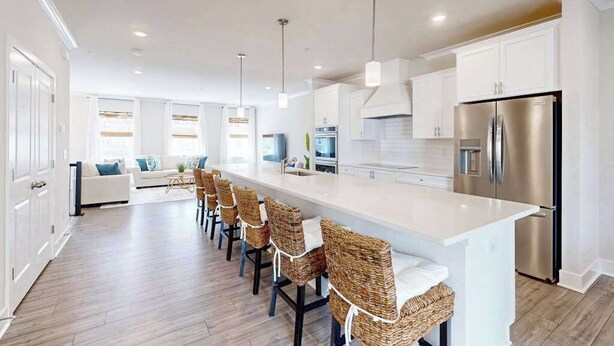 Een moderne keuken met een centraal eiland, roestvrijstalen apparatuur en een zithoek met rieten stoelen.