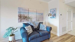 En stue med sofa, en potteplante og billedkunst på væggen.