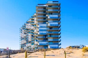 A multi-story building with balconies, situated on a sandy terrain. - Stunning-spacious condo, near the beach w/large balcony, AC, WiFi & shared pool (Ocean City)