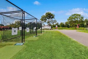 Un terrain d’entraînement de golf avec une zone d’entraînement protégée par un filet, une maison en arrière-plan et un panneau de signalisation indiquant un arrêt.