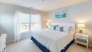 Un dormitorio con una cama, dos mesitas de noche con lámparas, una ventana con cortinas y un cuadro en la pared.