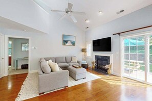 Un salon spacieux avec un canapé d’angle gris, une cheminée, un ventilateur de plafond et un grand téléviseur.