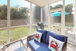 A covered outdoor seating area with a blue sofa, two cushions with crab designs, a grill, and a view of a backyard. - River Run 135 (Berlin)