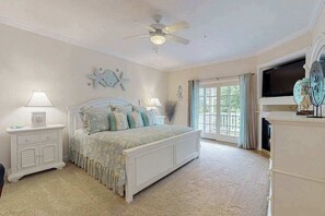Ein Schlafzimmer mit Bett, Nachttischen, Deckenventilator, großem Fenster und Kamin.