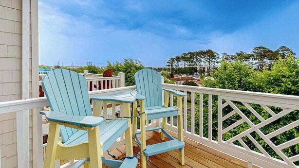 Une terrasse en bois avec deux chaises Adirondack et une rambarde blanche.