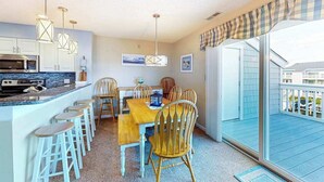 Une cuisine équipée d’un four à micro-ondes, d’une cuisinière et de tabourets de bar. On y trouve une table à manger avec des chaises, et la vue donne sur l’extérieur.