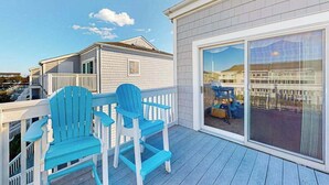 Un balcon avec deux fauteuils Adirondack bleus, une balustrade blanche et une grande porte-fenêtre coulissante donnant sur une terrasse.