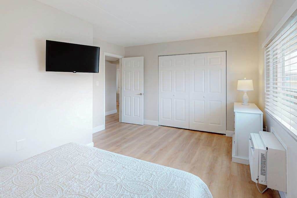 A bedroom with a bed, a television, a wardrobe, a radiator, and a window with blinds.