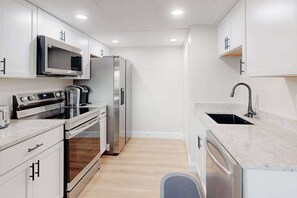 A modern kitchen with white cabinets, stainless steel appliances, a microwave, oven, and a sink. - Bali 202 (Ocean City)