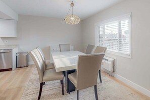 A dining area with a table and chairs, a hanging light fixture, a window with blinds, and a radiator. - Bali 202 (Ocean City)
