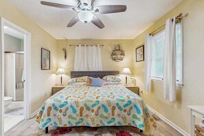 A bedroom with a bed, ceiling fan, bedside lamps, and a window with curtains. - Beach Retreat (Ocean City)