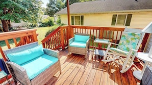 Eine Holzterrasse mit Korbmöbeln, darunter eine Couch und Stühle, sowie ein Schaukelstuhl.
