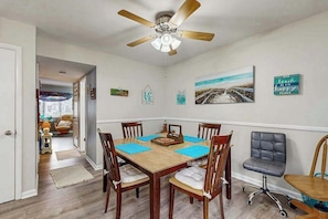A dining area with a wooden table, four chairs, a ceiling fan, and wall decorations. - Beach Retreat (Ocean City)