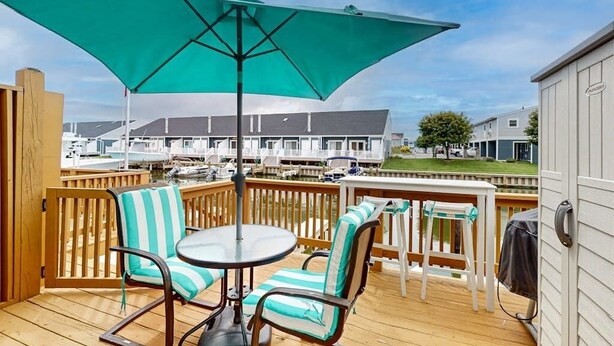 Um terraço com mesa e cadeiras, um grande guarda-sol e vista para uma marina com barcos.