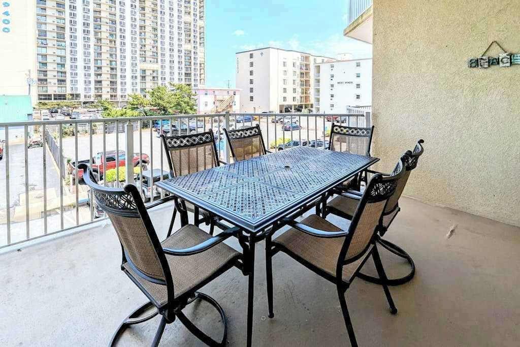 A balcony with a metal table and four chairs, a view of buildings, and a sign on the wall.