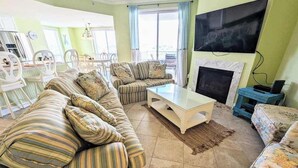 A living room with striped sofas, a coffee table, a fireplace, and a TV mounted on the wall. - Spacious - Family-Friendly Beach Condo w/Balcony, A/C, Shared Rooftop Pool & Gym (Ocean City)