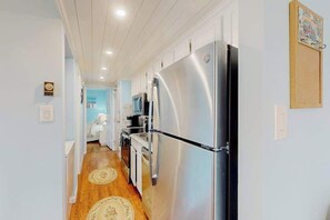 A narrow hallway with a stainless steel refrigerator, wooden flooring, and light blue walls. - Decatur House 305 (Ocean City)