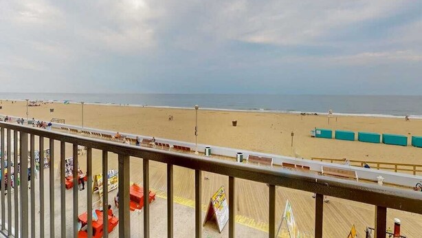 Vistes a la platja des d'un balcó amb barana, sorra daurada i cel serè.