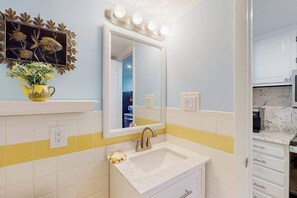 A bathroom with a mirror, vanity, and yellow-striped wall tiles. - Decatur House 305 (Ocean City)