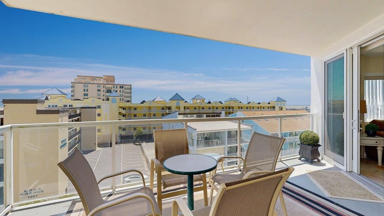 Ein Balkon mit Korbmöbeln, einem kleinen Tisch und Blick auf Gebäude in der Ferne.