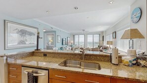 A spacious living area with a kitchen, large windows, and a view of the ocean. - Ocean-view condo with balcony, central AC, W/D, pool, gym & coastal decor (Ocean City)