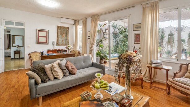 A living room with a grey sofa, wooden flooring, a coffee table with books and a vase, and a view of the outdoors through large windows. - Vacation Apartment 'Casa Tesalia' with Sea View, Wi-Fi and Air Conditioning (Güímar)