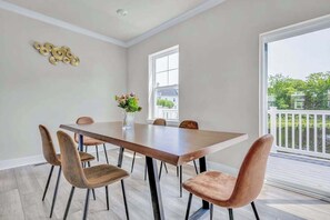 A dining area with a wooden table and chairs, a vase with flowers, and a window with a view of greenery.