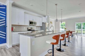 A modern kitchen with white cabinets, a granite countertop, and a bar area with wooden stools.