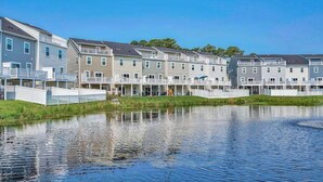 A row of modern multi-story buildings with balconies, a calm water body in the foreground, and a clear blue sky. - Sea Oaks Village 12442 #5 (Berlin)