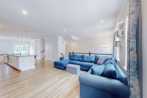 A spacious living area with a large L-shaped blue sofa, a kitchen island, and a staircase leading to another level.