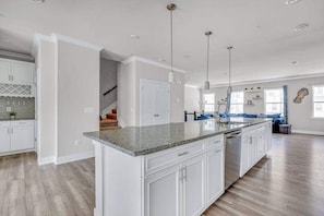 A spacious kitchen with white cabinetry, a granite countertop, and pendant lighting.