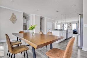 A modern kitchen with white cabinets, a wooden dining table, and a vase of flowers.