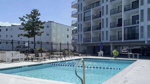 A swimming pool with lounge chairs, a fenced area, and a multi-story building with balconies. - Bluewater East 501N (Ocean City)